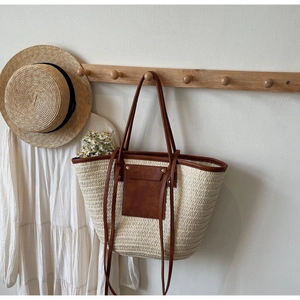 Detail of a large woven straw tote bag with brown leather pockets and long handles