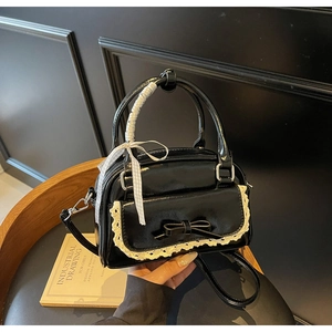Macro view of a black patent leather handbag featuring lace trim and a bow detail