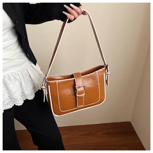 Detail view of brown croissant bag with contrast white edges and silver buckle accent