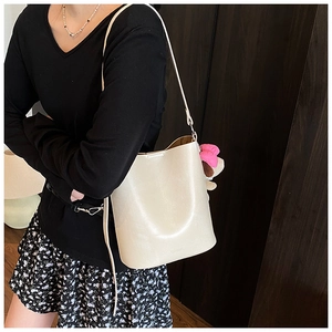 Detail of cream white leather bucket bag featuring SNML logo and cute plush bear charm