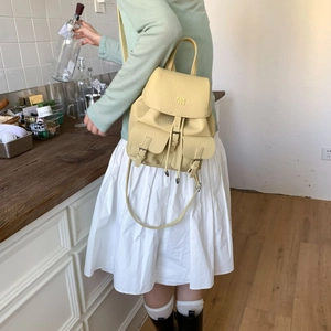 Detail view of a bright yellow pebbled leather backpack worn by a model in a home setting