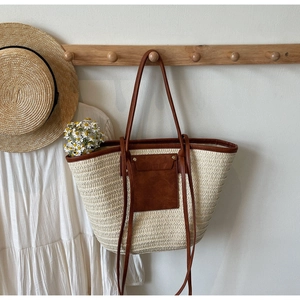 Detail of woven straw tote bag with brown leather pocket and long shoulder strap