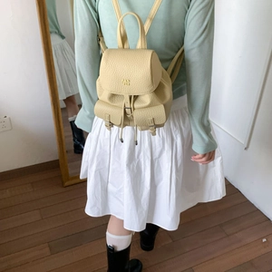 Close-up of light yellow pebble leather mini backpack with front pockets and metallic buckles
