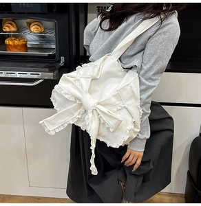 Dettaglio di una borsa a tracolla in tela bianca con fiocco grande e pizzo delicato