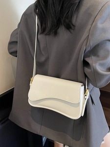 Sac à bandoulière blanc crème minimaliste avec rabat ondulé sur blazer gris élégant