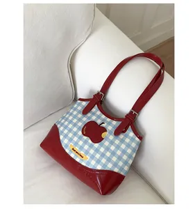 Detail of blue gingham tote bag featuring a red apple print and red leather handle