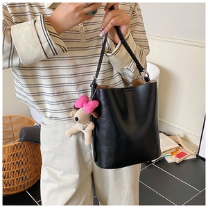 Detail of a black leather bucket bag with a cute pink bow plush dog charm accessory