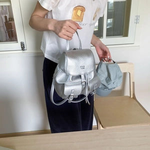 Detail of silver metallic textured mini backpack featuring drawstring and buckle accents