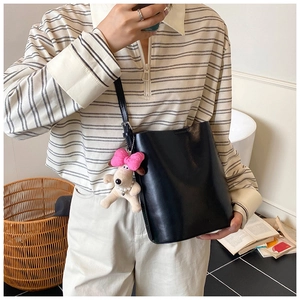 Detail of black leather bucket bag with cute beige puppy plush charm on striped shirt