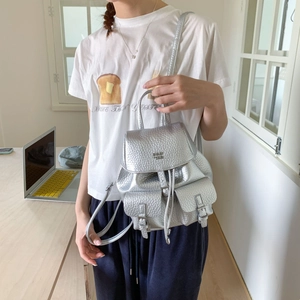 Silver metallic mini backpack with PAN TOR logo shown on a model in a modern indoor setting
