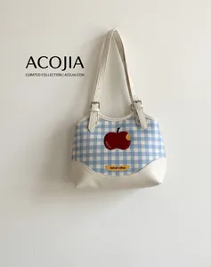 Detail of blue plaid tote bag featuring red apple embroidery and Not Anxious slogan