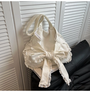Dettaglio di una borsa in tela bianca con un grande fiocco e bordo in pizzo delicato