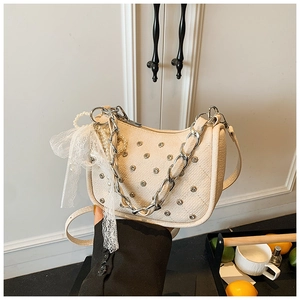 Détail du sac crème avec clous métalliques, breloques perles et nœud en dentelle