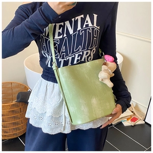 Detail of light green bucket bag with retro leather texture and cute bear pendant