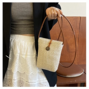 Detail view of mini straw bag with brown leather strap and decorative wood button closure