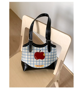 Detail of blue plaid fabric tote bag featuring red apple embroidery and black leather trim