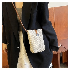 Detail of a beige woven mini crossbody phone bag with brown leather strap on a person