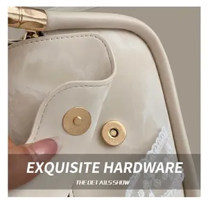 Detail of golden metal magnetic buckle and white lace trim on off-white crossbody bag