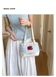 Close-up of blue and white plaid tote bag with red apple embroidery and leather strap