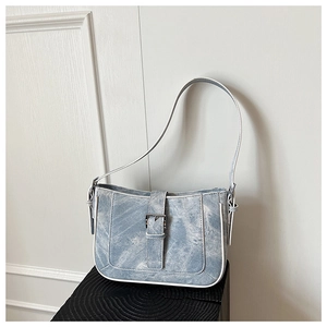 Close-up of light blue denim crescent bag featuring metal buckle and contrast white trim