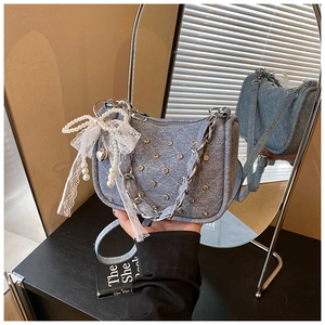Détail du sac bandoulière en denim bleu clair avec clous matelassés, perles et dentelle