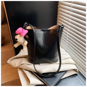 Detail view of a black leather bucket bag with a cute plush dog pendant and brand logo