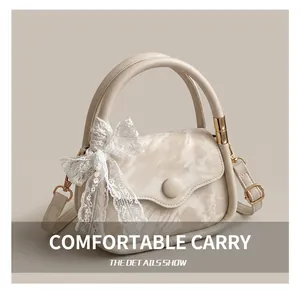 Detail of cream leather handbag handle featuring golden rings and white lace bow decoration
