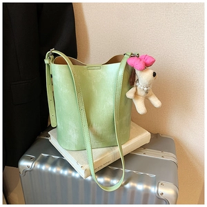 Detail of light green bucket bag with embossed logo and plush puppy charm