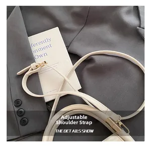 Detail showing adjustable leather shoulder strap with gold buckle on a beige bag