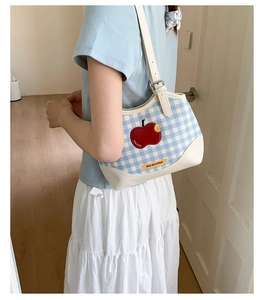 Detail of blue plaid underarm bag with red apple patch and adjustable shoulder strap