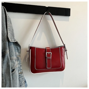 Detail of red crescent bag with white trim and silver buckle hanging on a rack