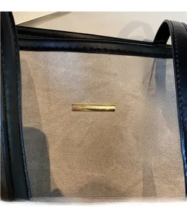 Detail of canvas tote bag with black leather handles and gold metal decorative bar