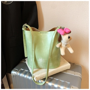 Detail of light green bucket bag with plush dog charm on a silver suitcase