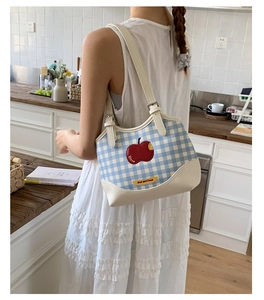 Blue plaid canvas tote bag with red apple patch worn over the shoulder in a kitchen