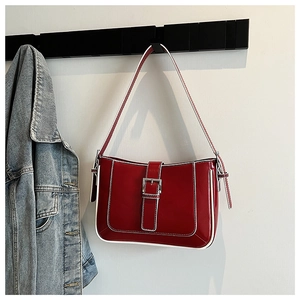 Red patent leather crescent bag with white edge trim and silver buckle on a wall hook