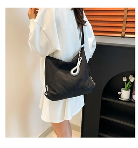 Détail du sac bandoulière en nylon noir avec tirette de zip blanche ronde sur la sangle
