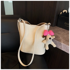 Detail of cream bucket bag featuring a plush puppy charm and embossed brand logo