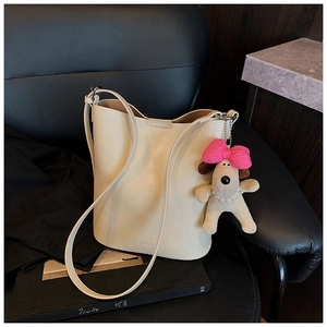 Detail of cream bucket bag with SNML engraving and cute plush dog charm on a leather chair