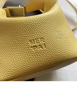 Close-up of yellow lychee grain leather handbag featuring embossed logo and soft texture