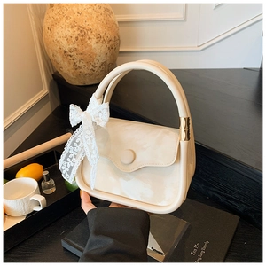 Detailed close-up of cream leather handbag featuring a white lace bow and gold hardware