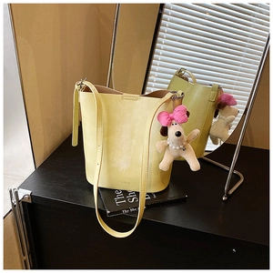 Detail shot of a yellow bucket bag featuring a cute plush dog pendant on a black surface