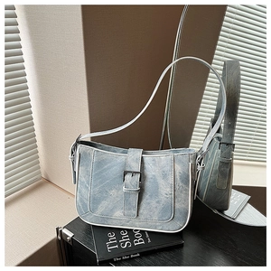 Close-up of blue denim crescent bag featuring metal buckle and white piping details