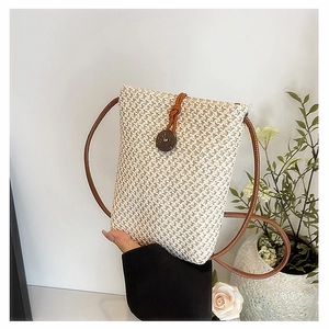 Detail of small straw woven crossbody bag with brown leather strap and wooden button