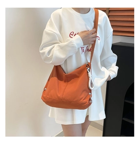 Détail du grand sac besace orange avec large bandoulière porté sur une tenue décontractée