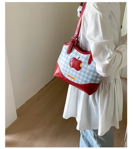 Detail of blue and white checkered tote bag with red apple patch and leather trim