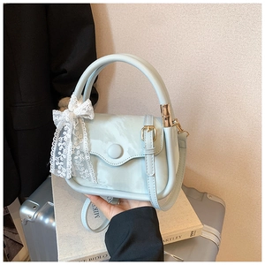 Detail of light blue crossbody bag with silk texture, lace bow, and gold hardware