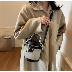 Detail of a chic bucket bag with beige canvas, black leather, and a floral silk scarf handle
