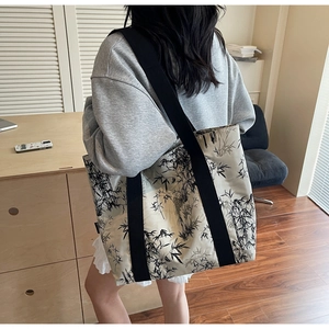 Detail view of large white tote bag with black bamboo leaf pattern on model shoulder