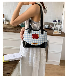 Detail of blue gingham canvas shoulder bag with red apple patch and leather strap