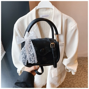 Detail of black mini handbag featuring a white lace bow and elegant gold metal clasp